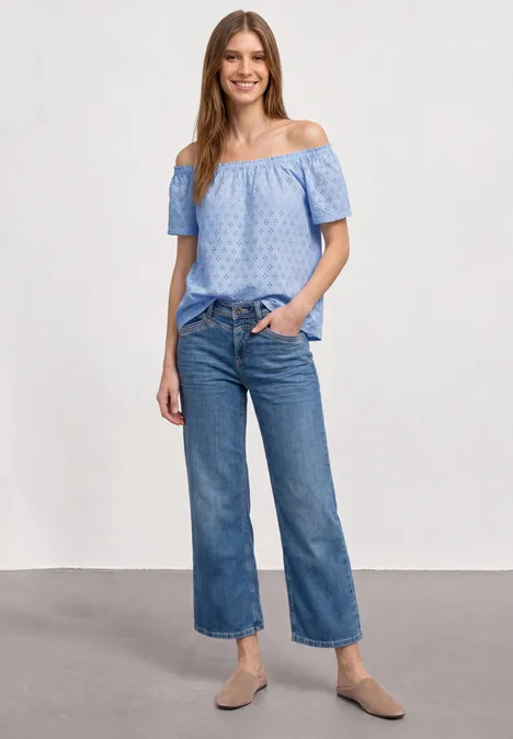 Carmen blouse cashmere blue Frau in schulterfreier, hellblauer Bluse, Culotte-Jeans und beigen Ballerinas vor neutralem Hintergrund.