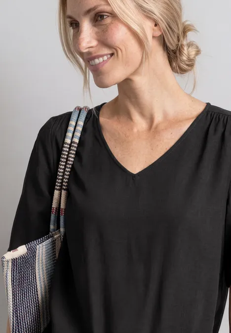 Frau trägt schwarzes V-Shirt und lächelt, hält bunten Schulterbeutel.