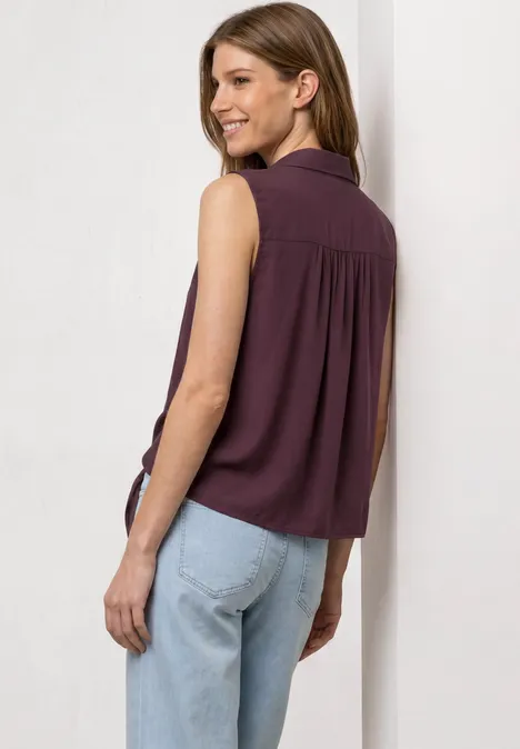 Blusentop mit Bowling-Kragen und Knoten rustic rouge Eine Frau von hinten in ärmelloser lila Bluse und hellen Jeans vor weißem Hintergrund.