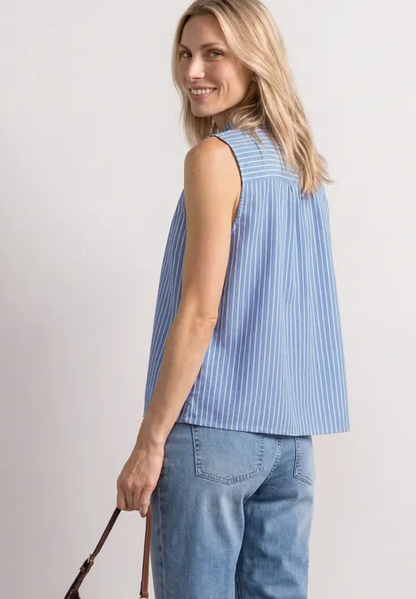 Een vrouw van achteren in een blauw-wit gestreept mouwloos topje met ringen bij de schouders en een spijkerbroek.
