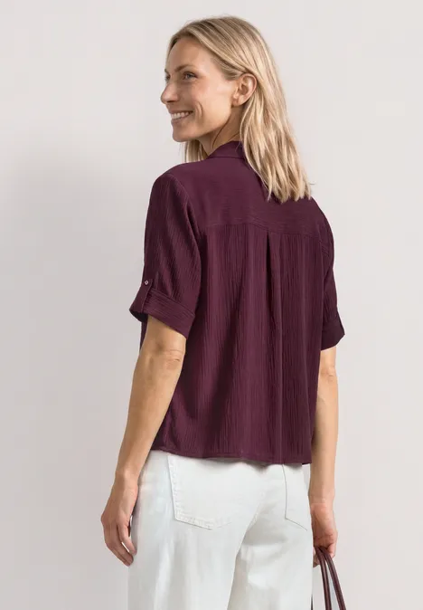 Vrouw van achteren met een paarse blouse, witte spijkerbroek en een tas in haar linkerhand.