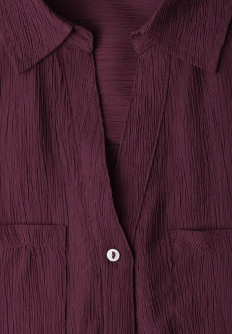 Close-up van een bordeauxroze, gestructureerd bloesje met kraag, V-hals, knoop en borstzakjes.