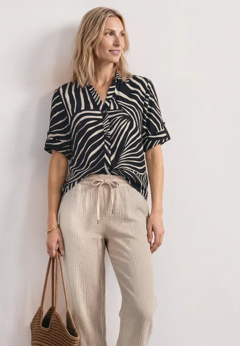 Vrouw met zwart-wit gestreepte top, beige linnen broek en bruine tas.