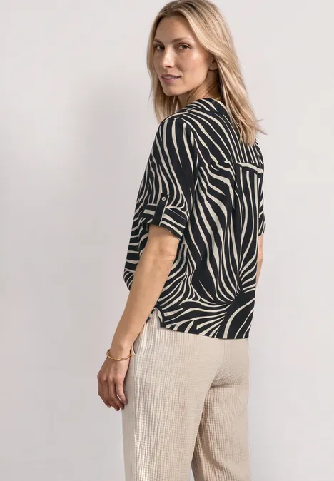Chemisier à manches courtes avec détails à revers Black Femme de profil portant un haut zébré noir et blanc et un pantalon ample beige