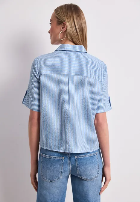 Kurzarm Hemdbluse mit Turn-Up-Details original blue Frau von hinten in hellblauer Kurzarmbluse und Jeans vor neutralem Hintergrund.