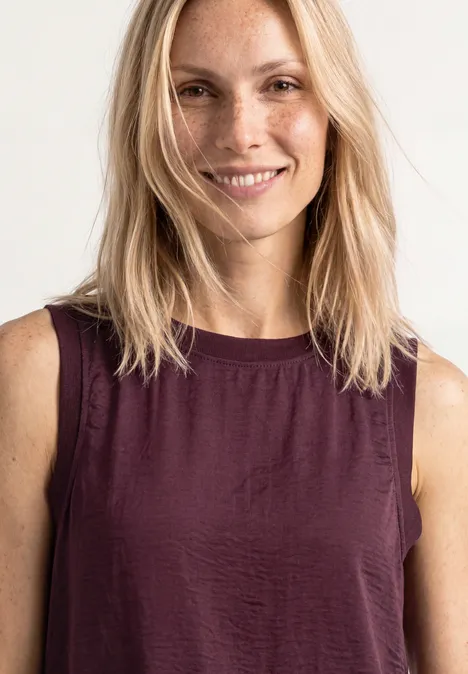 Blusentop mit Rundhals und Tape-Detail rustic rouge Frau mit schulterlangem blonden Haar in ärmellosem dunkelroten Top vor weißem Hintergrund.