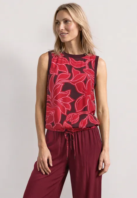 Frau in ärmellosem Top mit roten Blumen und passender roter Hose.