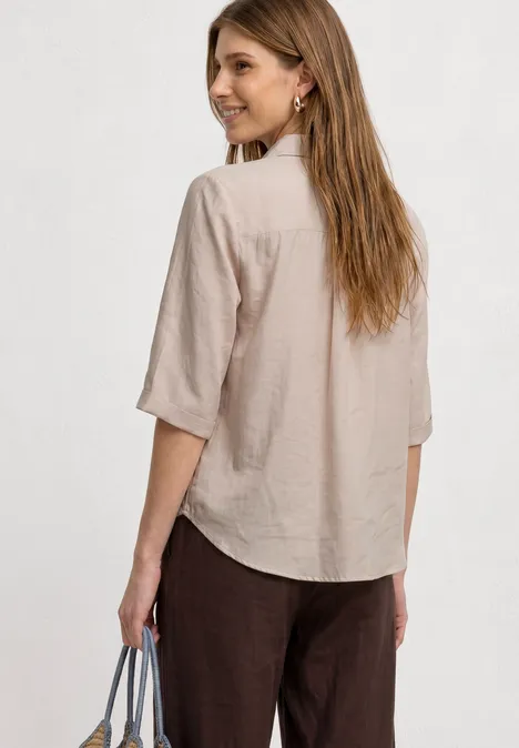 3/4-Arm Hemdbluse mit Brusttasche clay sand Frau von hinten in einer beigen Hemdbluse und dunklen Hosen, Handtasche in der Hand.