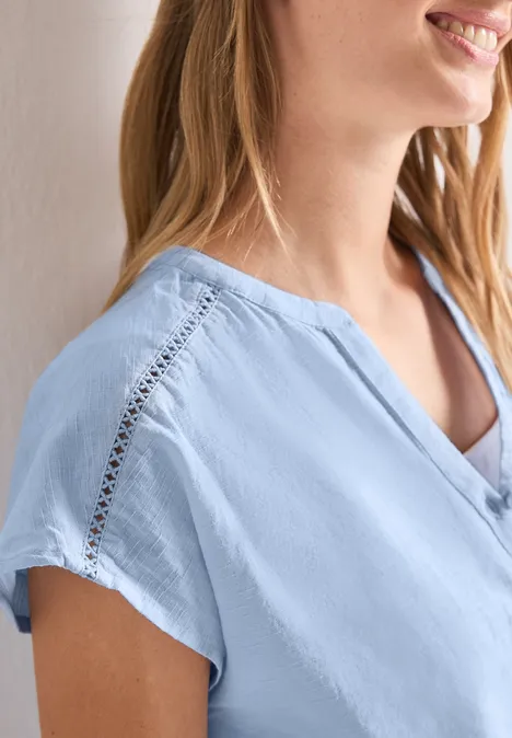 Vrouw in lichtblauwe blouse met kantdetail op de schouder en korte mouw