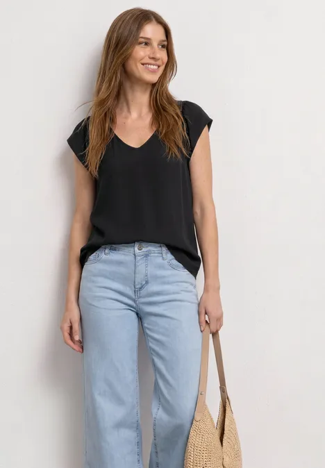 Dropped Shoulder Shirt mit V-Neck Black Frau trägt schwarzes V-Shirt, hellblaue Jeans und hält eine Strohtasche.