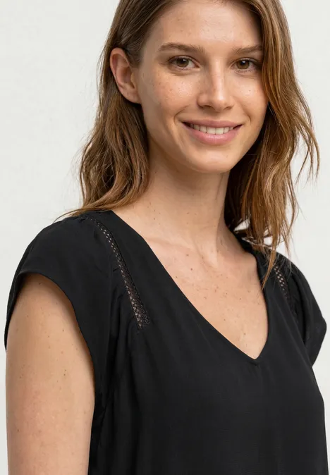 Dropped Shoulder Shirt mit V-Neck Black Eine Frau mit langen Haaren trägt ein schwarzes V-Ausschnitt-Oberteil.