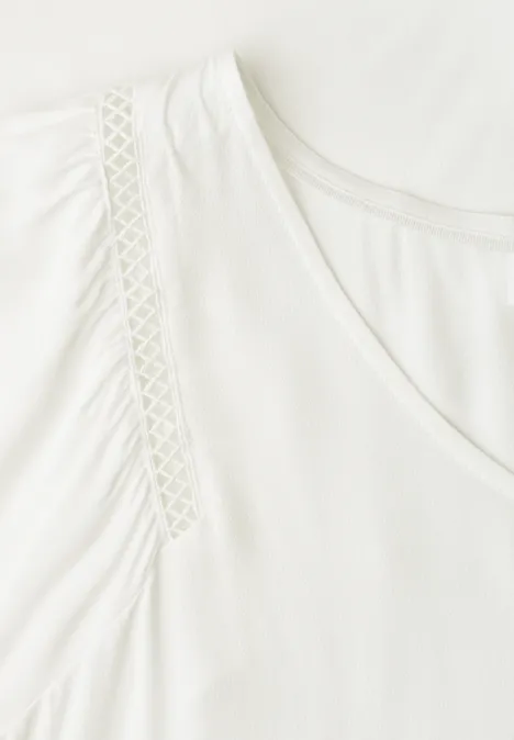 Weißes V-Ausschnitt-Shirt mit dekorativen Spitzen-Einsätzen an den Schultern.