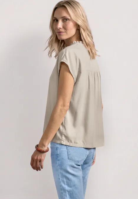 Zijaanzicht van een vrouw met blond haar, een beige top en lichtblauwe spijkerbroek voor een neutrale achtergrond.