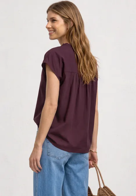 Vrouw van achteren in een bordeauxroze top en blauwe spijkerbroek, handtas in hand, neutrale achtergrond.