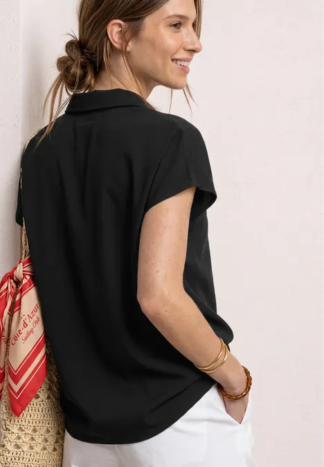 Frau seitlich, schwarzes T-Shirt, weiße Hose, Korbtasche mit rotem Tuch.