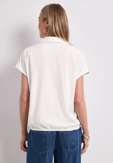 Blusenshirt mit Hemdkragen und Elastiksaum off white Rückansicht einer Frau in weißer kurzärmeliger Bluse mit Kragen, locker tailliert, dazu blaue Jeans.