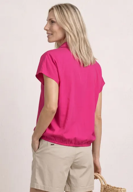Frau von hinten in pinkem T-Shirt und beigen Shorts vor hellem Hintergrund.