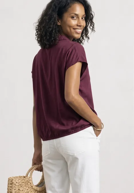 Blusenshirt mit Hemdkragen und Elastiksaum rustic rouge Eine Frau steht seitlich, trägt ein weites bordeauxrotes Oberteil, weiße Hose und hält eine Korbtasche.