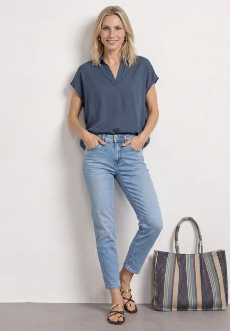 Blouseshirt met overhemdkraag en elastische zoom null Vrouw met onscherp gezicht, draagt een blauw topje en lichtspijkerbroek, staat naast een gestreepte tas.