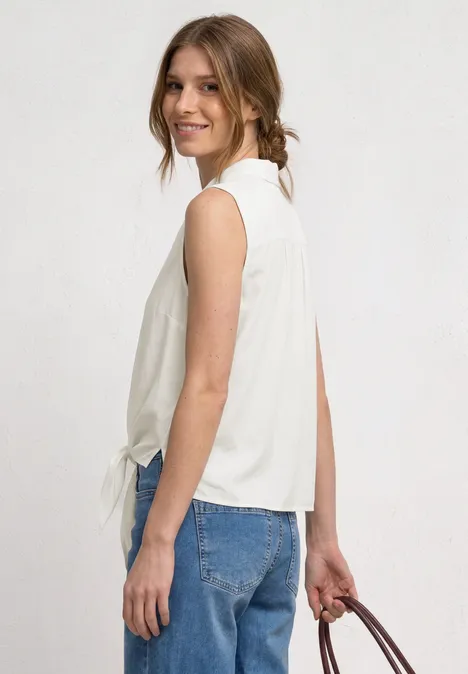 Blusentop mit Bowling-Kragen und Knoten off white Frau in weißem ärmellosem Oberteil und blauen Jeans, seitlich stehend und Handtasche in der Hand