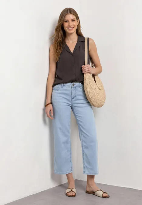 Blusentop mit Bowling-Kragen und Knoten espresso brown Frau in dunklem ärmellosem Top, hellblauen Jeans, braunen Sandalen und Strohtasche vor weißem Hintergrund.