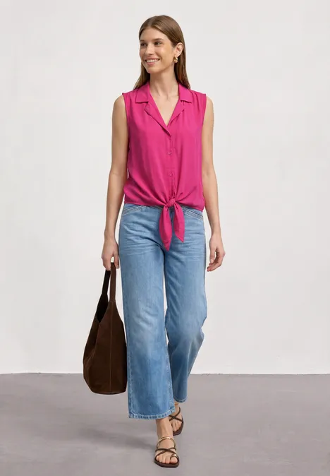 Blusentop mit Bowling-Kragen und Knoten magenta dream Frau in pinkem, ärmellosem Oberteil, das vorne geknotet ist, trägt weite blaue Jeans, Sandalen und eine braune Tasche.