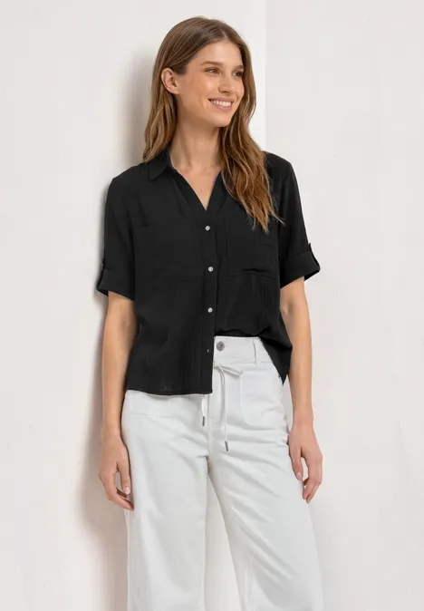 Een persoon draagt een zwart kort mouw shirt en een witte broek tegen een witte achtergrond.