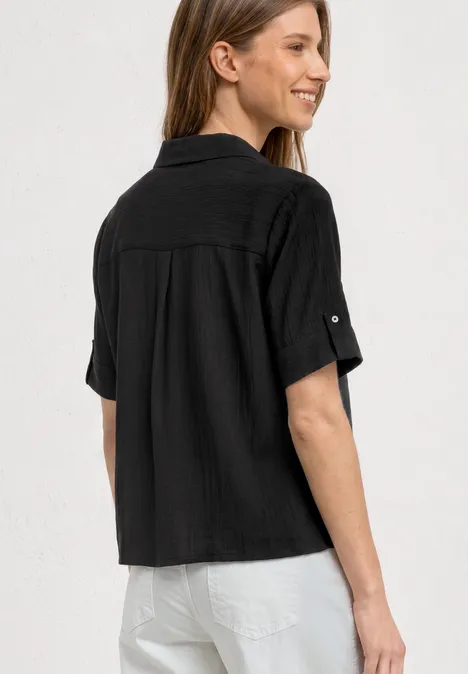 Achteraanzicht van een persoon met een zwart, kort mouwen hemd en een witte broek.