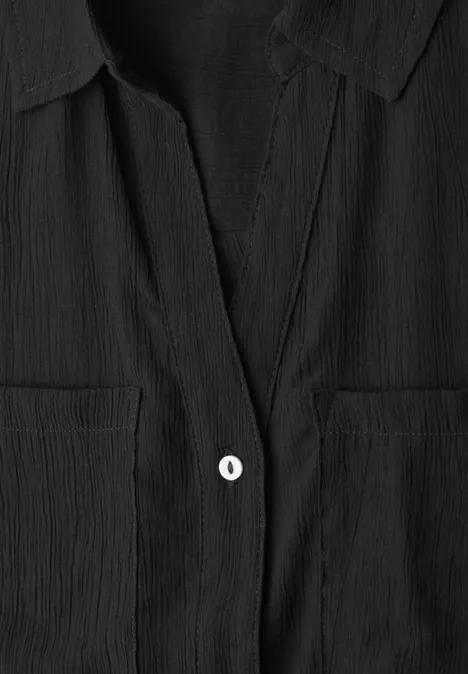 Close-up van een zwarte gestructureerde blouse met kraag en een witte knoop.