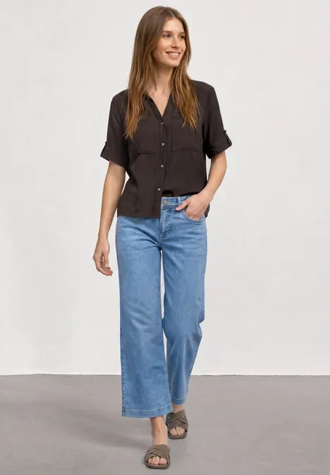 Kurzarm Hemdbluse mit Turn-Up-Details espresso brown Frau in schwarzem kurzärmeligem Hemd, weiten blauen Jeans und Sandalen vor neutralem Hintergrund.