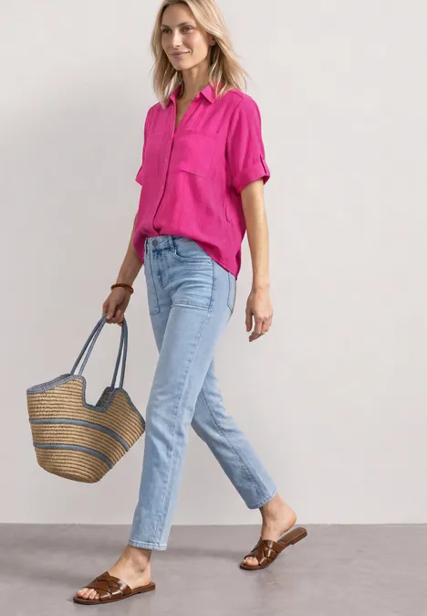 Overhemd met korte mouwen en omgeslagen manchetten magenta dream Vrouw in roze blouse en lichtblauwe jeans met strooien tas en bruine sandalen.