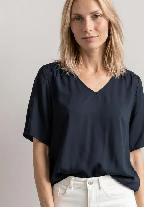Blouseshirt met korte mouwen en V-hals shadowed navy Vrouw in zwart V-halsshirt en witte broek, torso zichtbaar.