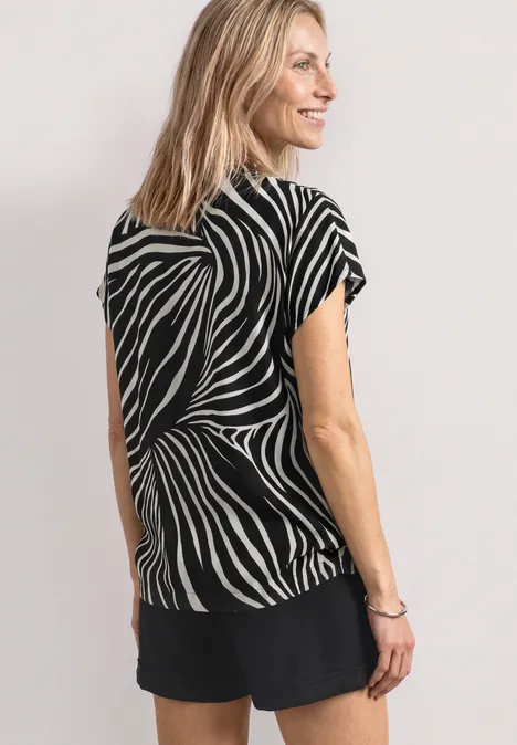 Vrouw van achteren in een zwarte short en een zwart-wit zebrapatroon top, lichte achtergrond.