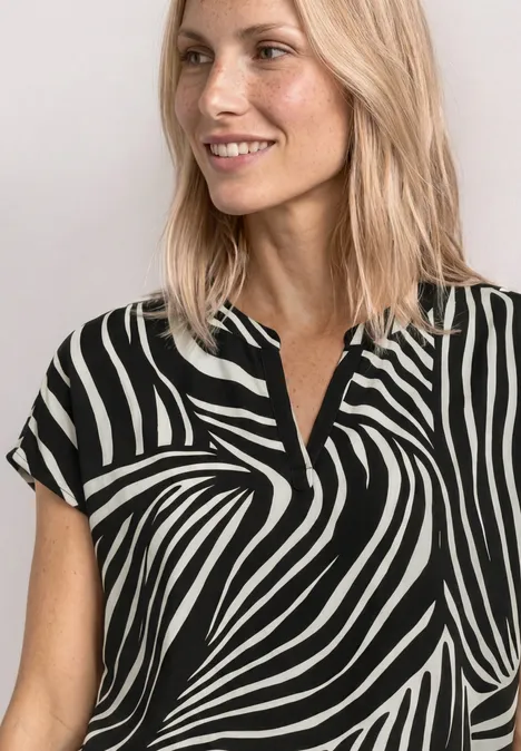 Een glimlachende vrouw met blond haar draagt een kort mouw blouse in zwart-witte zebraprint.