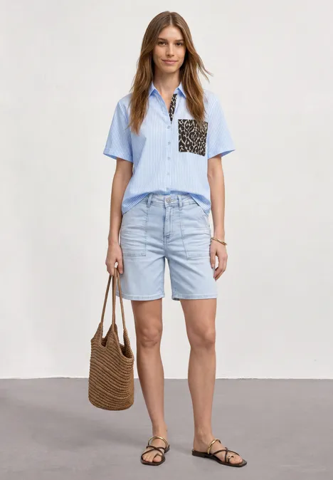 Kurzarm Hemdbluse mit Leo-Details original blue Eine Frau in hellblauem Hemd mit Leopardenprint-Tasche, Jeans-Shorts, schwarzen Sandalen und Korbtasche.