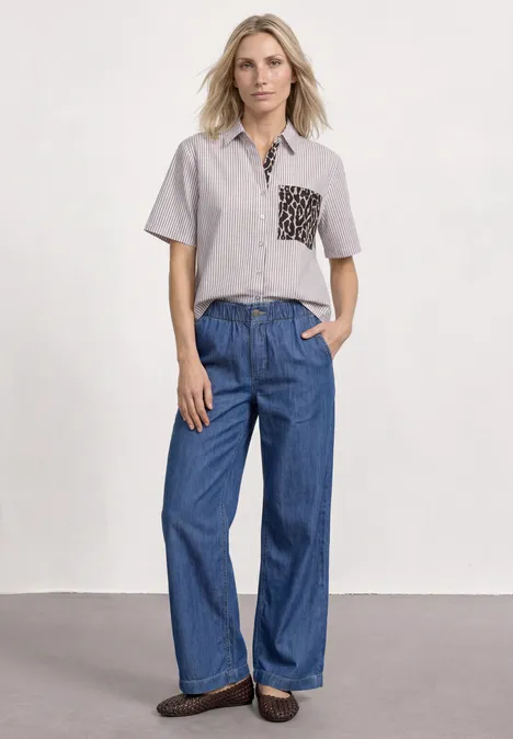 Kurzarm Hemdbluse mit Leo-Details light terra mocha Person trägt kurzärmliges Hemd mit gemusterter Brusttasche, weite Jeans und braune Schuhe vor neutralem Hintergrund.