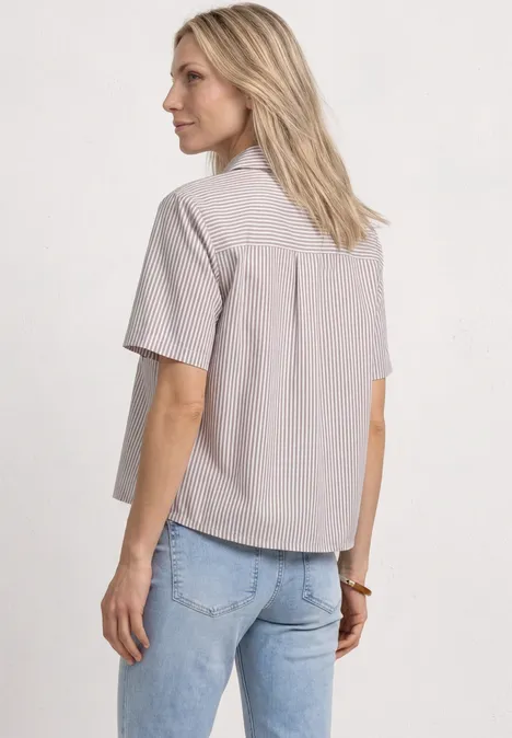 Kurzarm Hemdbluse mit Leo-Details light terra mocha Frau in hell gestreiftem Kurzarmhemd und blauer Jeans, von hinten vor neutralem Hintergrund.