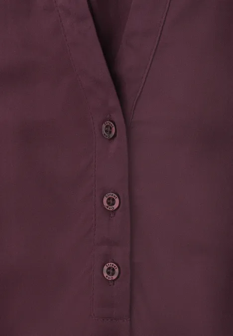 Donkerrode blouse met V-hals en drie zichtbare knopen.