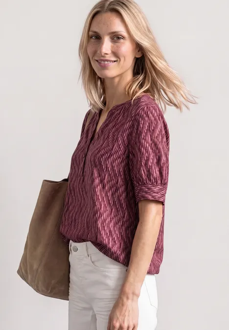 Blouse met korte mouwen, gespleten hals en elastische zoom blush berry Vrouw in paars shirt en witte broek met grote tas tegen een lichte achtergrond.