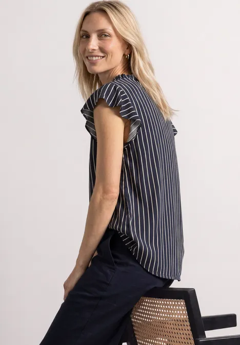 Blonde Frau im gestreiften Top sitzt seitlich auf einem Stuhl und lächelt zur Kamera.