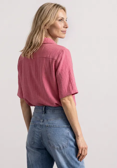 Mousselineblouse met bowlingkraag blush berry Vrouw van achteren in roze blouse met korte mouwen en blauwe spijkerbroek.