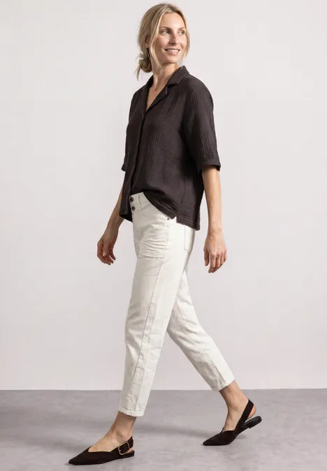 Mousselineblouse met bowlingkraag black coffee Vrouw in zwarte blouse, lichte broek en zwarte slingback-pumps voor een neutrale achtergrond.