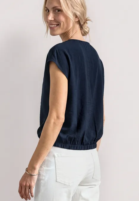 Blusenshirt mit Rundhals und Schnallendetail darkest blue Rückansicht einer Frau in dunkelblauem Kurzarmshirt und weißer Hose, Haar zu einem Dutt frisiert.