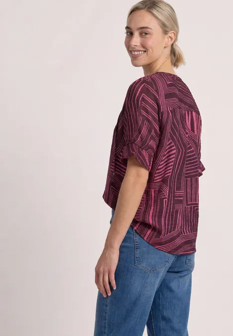 Blouse met korte mouwen, split in de hals en print blush berry Vrouw in zij-aanzicht draagt een losse, paars gemêleerde top en spijkerbroek, ze lacht.