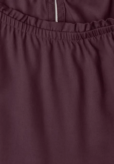 Nahaufnahme eines burgunderfarbenen Kleidungsstücks mit elastischem Bund und Reißverschlussdetail.