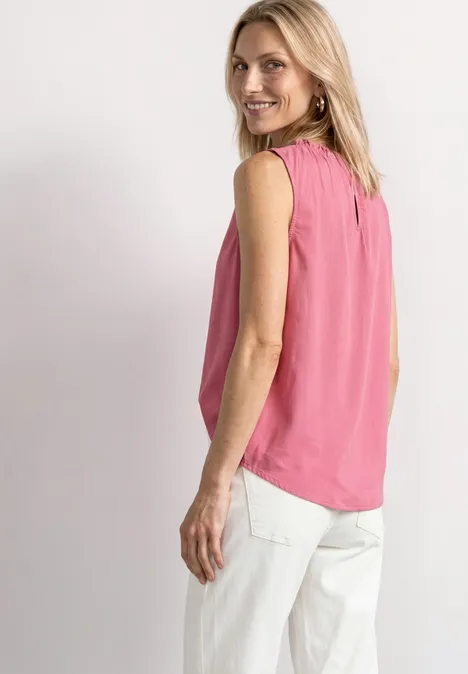 Blouse met gerimpelde ronde hals blush berry Blonde vrouw in mouwloze roze top en witte broek, zijwaarts pose, glimlachend terugkijkend naar de camera.