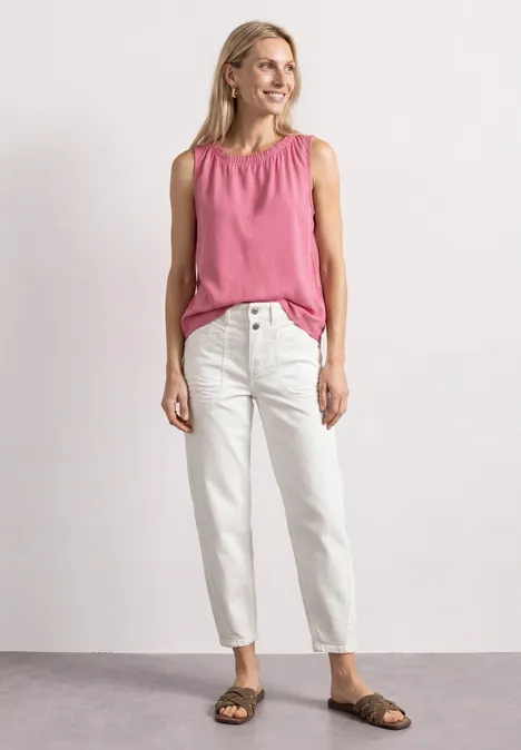 Blouse met gerimpelde ronde hals blush berry Vrouw in een mouwloze roze top, witte jeans en bruine sandalen, staand en glimlachend voor een lichte achtergrond.