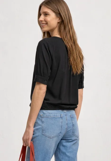 Kurzarm Bluse mit Split Neck und Elastiksaum Black Frau von hinten in schwarzer Bluse, blauen Jeans und mit einer roten Tasche.