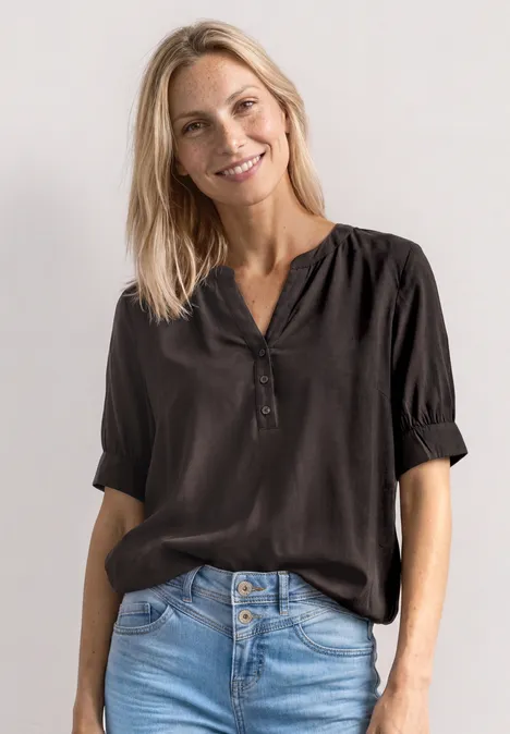 Blouse met korte mouwen, split in de hals en elastische zoom black coffee Frau trägt schwarze Bluse mit halblangen Ärmeln und hellblaue Jeans, Oberkörperaufnahme.