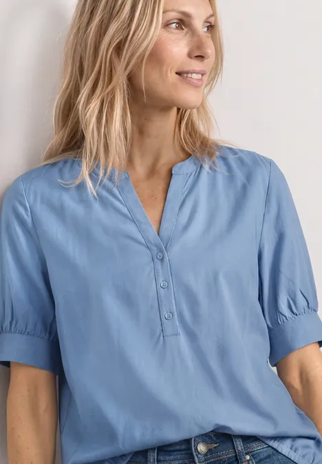 Blouse met korte mouwen, split in de hals en elastische zoom northern blue Frau in hellblauer Bluse mit kurzen Ärmeln, V-Ausschnitt und Knopfleiste, lässig posierend.